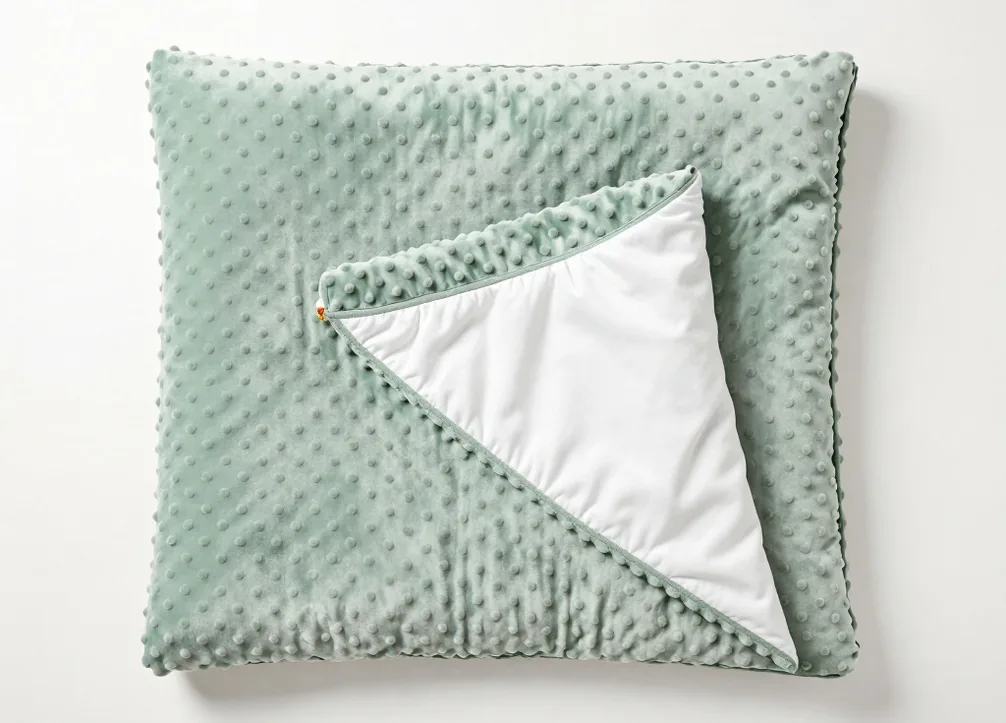 Top-down flat lay of a weighted blanket with sage green minky dot texture partially folded back